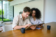 © Dorde - An African American woman and her Caucasian partner sit at a table with a focused gaze on a digital tablet, enjoying technology in a bright, modern home.