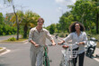 © Dorde - A cheerful African American woman and her Caucasian partner stroll with bikes along a sunlit path, dressed casually for their leisurely outdoor activity.