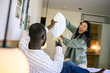 © Dorde - A joyful black male and Asian female engage in a light-hearted pillow fight, their smiles suggesting a carefree domestic moment in a cozy home setting.