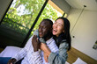 © Dorde - A smiling Black male and Asian female relax together, their casual wear suggesting comfort in their shared space, a home environment filled with natural light and greenery.