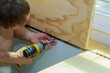 © ungvar - Worker is focused on securing plywood panels hinges to surface using power drill.