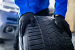 © zphoto83 - A mechanic in a blue jacket is lifting a tire in a garage during the morning, preparing for vehicle maintenance and repairs
