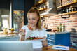 © Geber86 - Woman using laptop on kitchen table while eating healthy meal