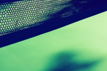 A close-up of a black mesh net casting a shadow on a green surface.