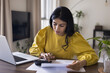© fizkes - Focused busy Indian freelance accountant woman checking financial documents, counting budget, income, expenses on calculator, sitting at home workplace table with laptop. Homeowner reviewing invoices