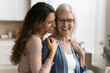 © fizkes - Tenderness between older mother and her millennial daughter, standing together in domestic kitchen smiling, hugging, laughing while remembering cherished life moments. Familial ties, love and support