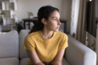 © fizkes - Serious thoughtful attractive 20s Latin woman looking at window away in deep thoughts, sitting on sofa, thinking on problem solving at home. Concerned pensive Hispanic young adult girl casual portrait