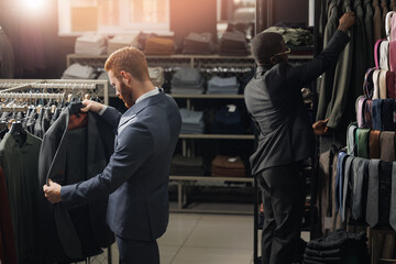 Wall Mural - Two mans buyers in fashionable suit chooses jackets and tie in men clothing store