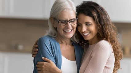 Wall Mural - two multigene rational women standing indoor and cuddling tightly. mature mother embraces her beauti