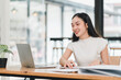© PRIME STOCK LAB - woman smiles while working on laptop at modern office desk, surrounded by papers and small plant. Her focused expression reflects productivity and engagement