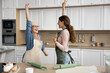 © fizkes - Lively older woman and millennial daughter wear aprons dancing in kitchen, moving to favourite music with arms raised, feel happiness, looking carefree, while preparing home-made holiday cake at home