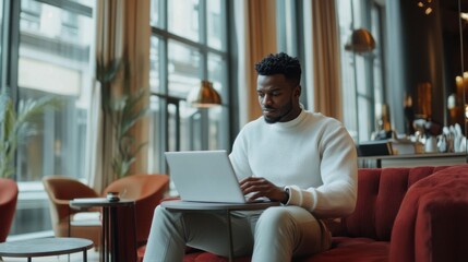 Poster - A man is sitting on a red couch and using a laptop