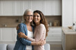 © fizkes - Strong family ties, multigenerational relatives love, and emotional, mutual support, close relationships. Senior 65s woman and young 35s daughter standing together at home embracing, look at camera