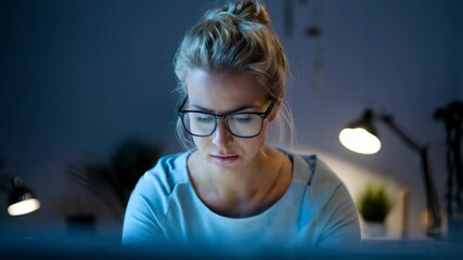 Poster - A focused woman working on a laptop in a dimly lit room.