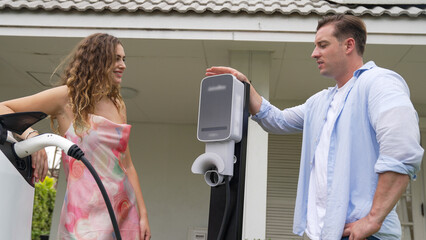 Happy and lovely couple with eco-friendly conscious recharging electric vehicle from EV charging station. EV car technology utilized as alternative transportation for future sustainability. Synchronos