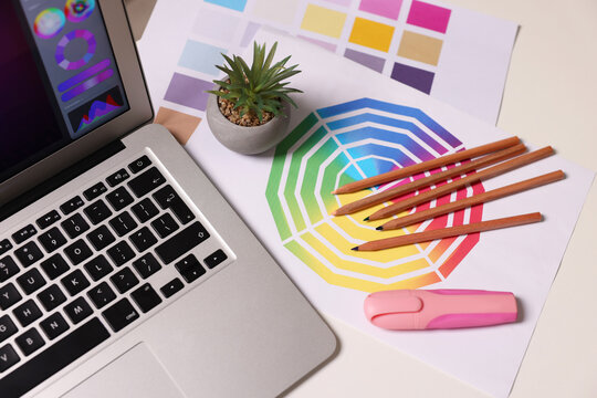Designer's workplace with laptop, stationery and palettes on white table, above view
