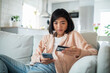 © Davor - Asian woman using credit card on smartphone from home couch