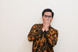 © Nurma - A shocked Southeast Asian man wearing batik shirt and glasses isolated over white background, Positive person, for an advertisement.