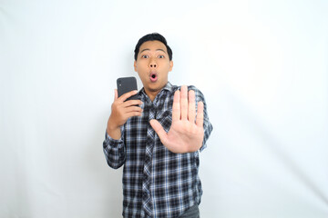 surprised and shocked asian man showing stop and warning gesture using hand with holding mobile phone isolated on white