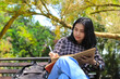 © M Alfan Setyawan - beautiful asian young woman college student focused writing on notebook and reading book in outdoors city park