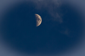 The moon in the dark blue sky with white clouds, closeup