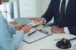 © Kritdanai - Legal Settlement: Close-up shot of a lawyer handing a stack of cash to a client, representing the concept of financial compensation for a legal case.