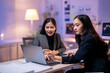 © Apichat - Two women are sitting at a desk with a laptop in front of them