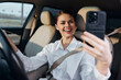 © SHOTPRIME STUDIO - Selfie, woman, car, driver's seat, smiling a woman sits in the driver's seat of her car, smiling and looking at the camera while taking a selfie with her cell phone