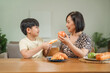 © NanSan - A mother and son happily feed each other snacks while sitting at the table in their house. They share joyful moments, bonding through play and enjoying their family time together