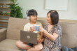 © NanSan - An Asian mother and son sit at the table and sofa, sharing time together while looking at a computer, tablet, and phone. They bond through technology and family activities