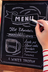 Wall Mural - Woman drawing christmas menu of cocoa bar on small chalkboard.