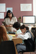 © pressmaster - Group of clever intercultural schoolkids sitting by table in classroom and writing down English grammar rules in copybooks
