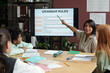 © pressmaster - Young smiling teacher looking at group of schoolkids and pointing at interactive board with English grammar rules