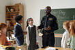 © pressmaster - Young African American security guard or policeman surrounded by cute intercultural schoolchildren talking about his career