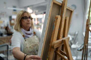 Focused senior woman artist preparing easel in art class