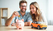 © Radorog. - a happy young couple throws a coin into a piggy bank, next to it is a model of a car, a concept of savings for the purchase of real estate