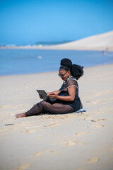 Wall Mural - Woman seen sitting at the beach and using laptop