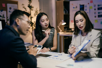 Wall Mural - Asian businesspeople working late in modern office, analyzing financial data and brainstorming new strategies for project