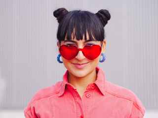 Wall Mural - Latin america woman whit love heart red shape sunglasses and buns hairstyle, front portrait. Pink clothes. Valentine's day, 14 february love, friendship and emotion concept. hispanic brunette  ecuador