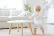 © Natalia - Baby standing for the first time in a modern living room while holding onto a coffee table in bright sunlight