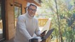 © nyul - Mature businessman using laptop and smartphone on wooden terrace of mountain chalet, remote working from peaceful nature. Portrait of happy mid adult man wit grey hair and glasses, smiling.