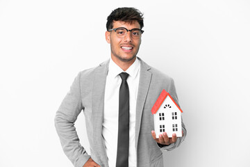 Poster - Business man holding a house isolated on blue background posing with arms at hip and smiling