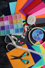 DIY project in making. Top view photo of colorful glass beads, felt fabric and scissors on dark grey desk. Handwork in process. 