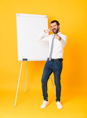 Wall Mural - Full-length shot of businessman giving a presentation on white board over isolated yellow background making phone gesture and pointing front