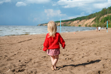 Caucasian little child girl two-year-old in dress on a sea beach in summer, sstkbabies. Family vacation, cold season.