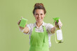 © Alliance - happy female in green apron and rubber gloves against green