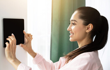 Aufkleber - Young woman controlling house with a digital touch screen panel installed on the wall in the living room. Concept of a smart home and mobile application for managing domestic devices, mockup