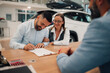 © Zamrznuti tonovi - Content couple signing car purchase agreement at dealership table.