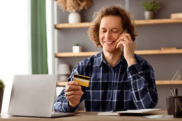 Poster - Cheerful Man Holding Credit Card Calling To Bank Via Smartphone Pleased With Banking Service For Online Shopping Sitting In Modern Office. E-Commerce, Finances And Payments. Selective Focus