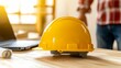 © PixelPlace - Construction hard hat, blueprints, laptop. A bright yellow hard hat rests on a wooden table next to a laptop, symbolizing construction safety and workplace readiness.